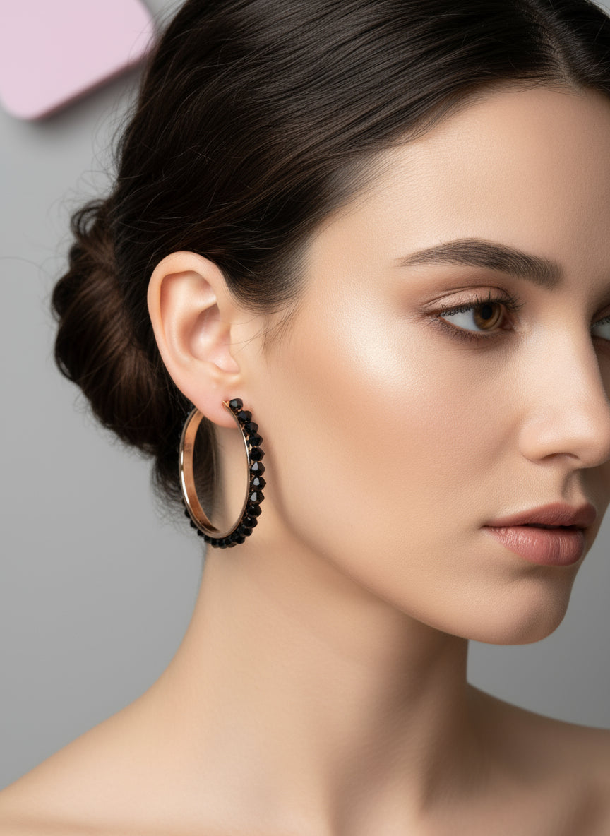 Close-up of a woman wearing gold hoop earrings with black beads on a gray background