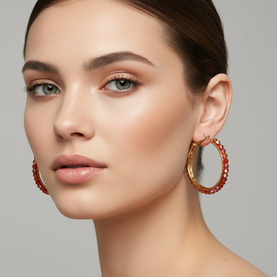 Gold hoop earrings with red beads on a silver background