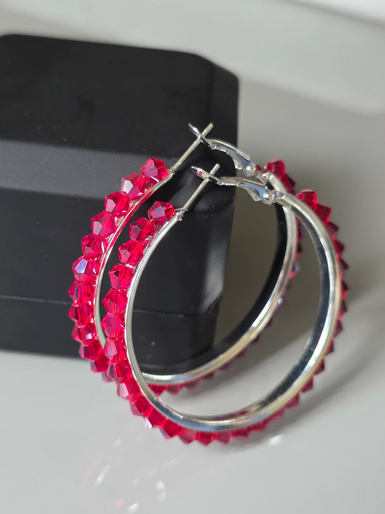Silver hoop earrings with red gemstones on a white surface