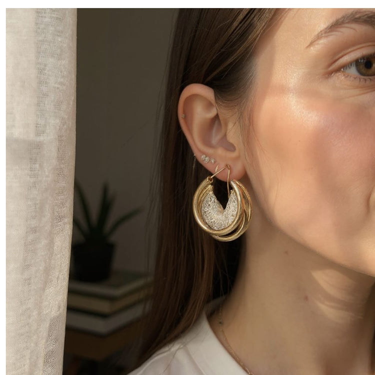 Close-up of a woman wearing gold hoop earrings with a blurred indoor background